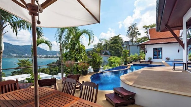 An outdoor pool area with a wooden deck, lounge chairs, and a view of the sea and mountains. - Pra Nang (Phuket)