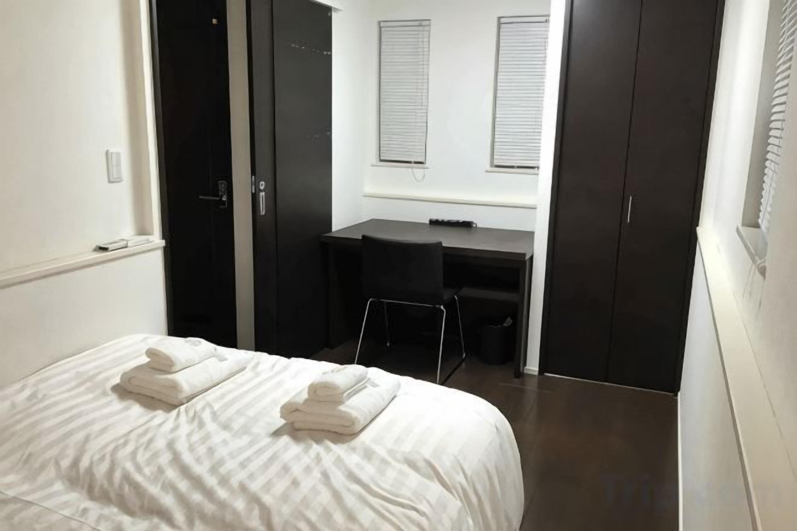 A bedroom with a bed, a desk, and a wardrobe.