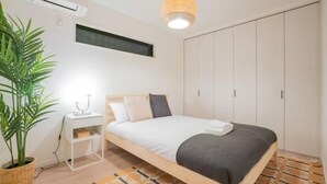 Une chambre moderne comprenant un lit, une table de chevet, une plante en pot, une armoire et un luminaire suspendu.