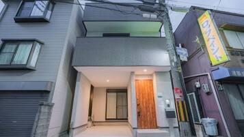 A modern two-story building with a flat roof, a wooden door, and a visible staircase leading to the entrance.