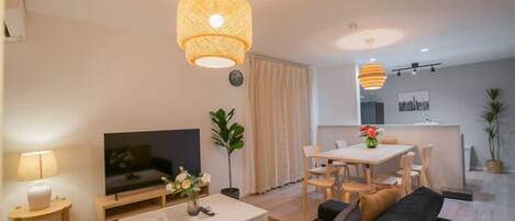 A modern living room with a sofa, coffee table, TV, and a dining area with a table and chairs.
