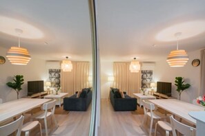 A modern dining area with a central sofa, white chairs, and pendant lighting. - Seiwa・Travel Time Sunahama｜Direct train access to Namba and Shinsaibashi (Osaka)