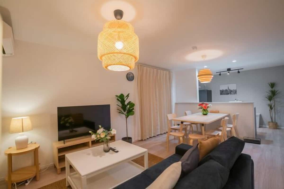 Ein modernes Wohnzimmer mit Fernseher, Sofa, Couchtisch und Essbereich mit Stühlen.