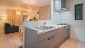 Une cuisine moderne dotée d’un îlot central, d’un four encastré et d’un four à micro-ondes. On y trouve également un coin repas avec une table et des chaises, ainsi qu’un salon avec un canapé et une lampe.
