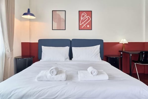 A hotel room with a large bed, two side tables, a desk, and a lamp.