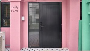 A pink exterior wall with a dark door and a small window. The text "Emily Home" is visible on the wall. - Emily Home 3BR Old Town Chiang Mai by Beginning With (Chiang Mai)
