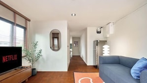 A modern living room with a flat-screen TV, a blue sofa, and a wooden entertainment unit. - Emily Home 3BR Old Town Chiang Mai by Beginning With (Chiang Mai)
