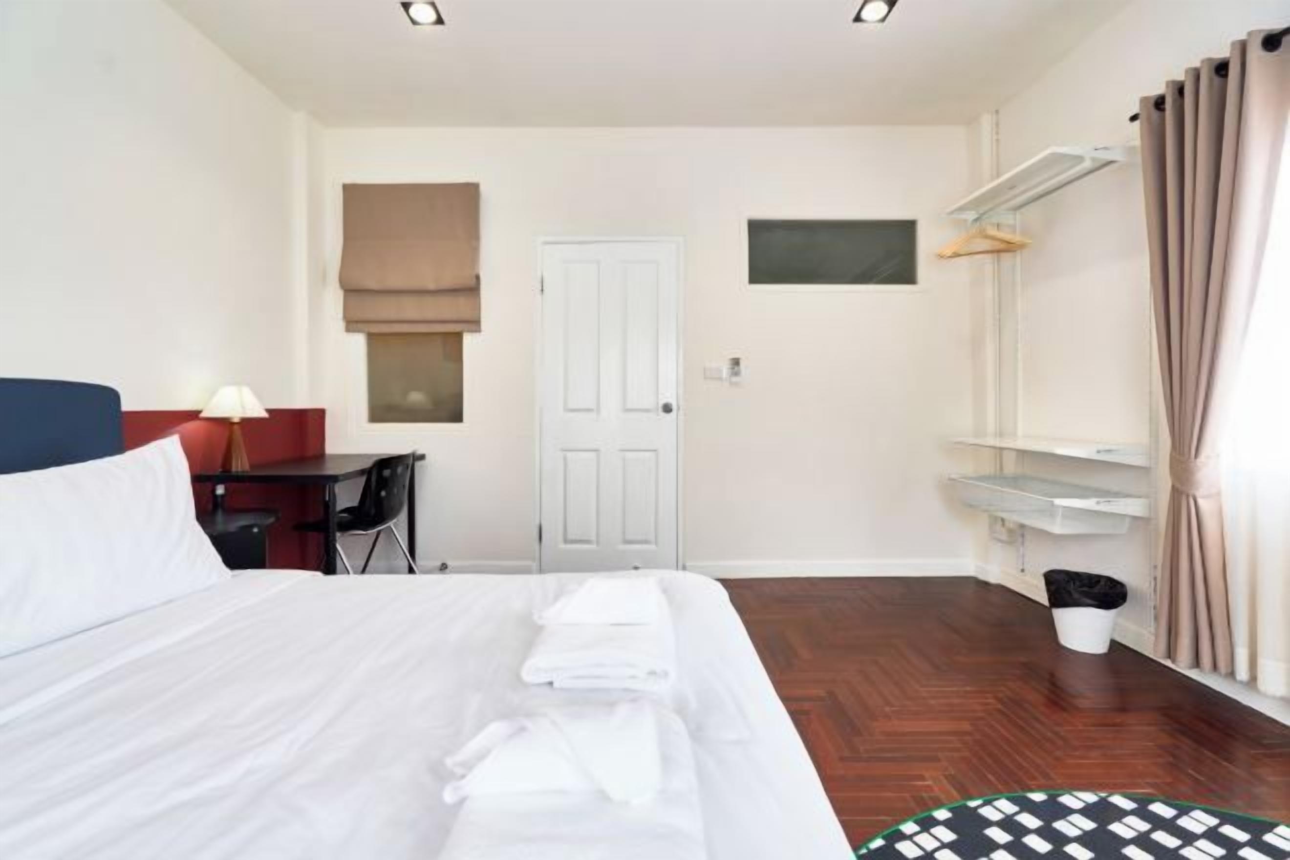 A hotel room with a bed, a desk, a chair, a wardrobe, a mirror, and a window with curtains.