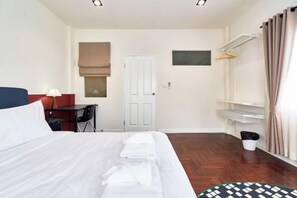 A hotel room with a bed, a desk, a chair, a wardrobe, a mirror, and a window with curtains. - Emily Home 3BR Old Town Chiang Mai by Beginning With (Chiang Mai)