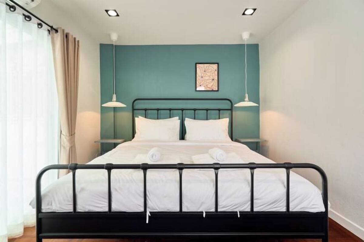 A bed with white linens, a teal wall, and two pendant lights.