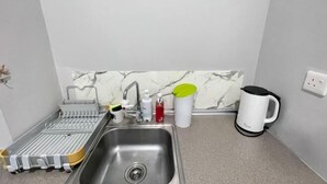 A kitchen with a stainless steel sink, a dish drying rack, a kettle, and a marble backsplash. - Jesselton Quay Central Citypad (Kota Kinabalu)