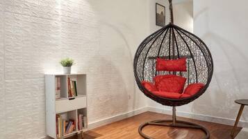 A room with a white textured wall, a wooden floor, a white bookshelf with books, and a red cushioned hanging chair.