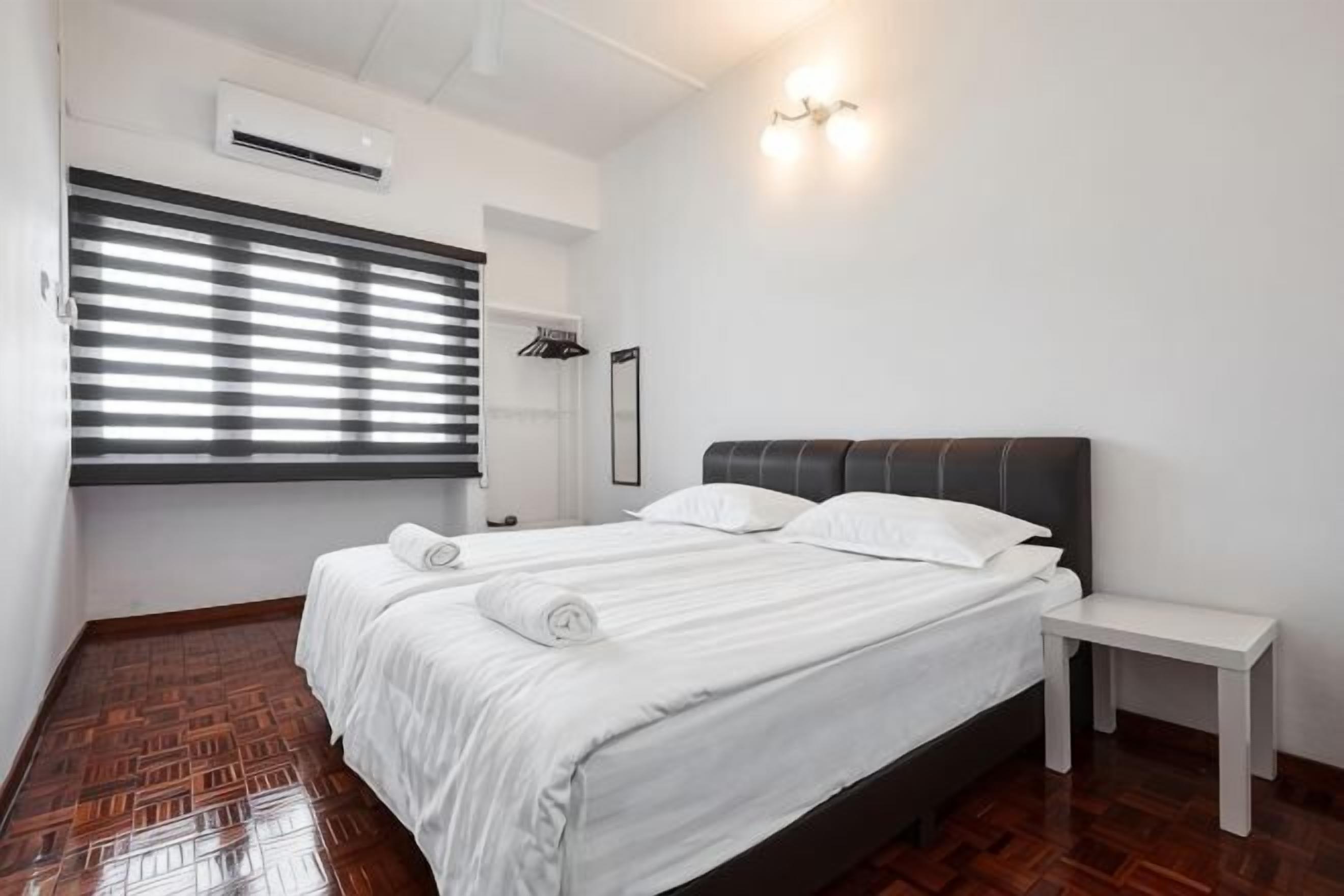 A bedroom with a bed, bedside table, and a window with blinds.