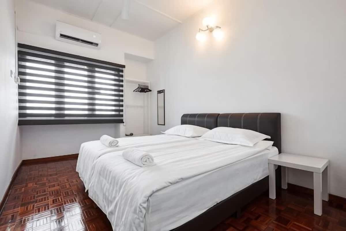 A bedroom with a bed, bedside table, and a window with blinds.
