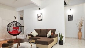 A modern living room with a sectional sofa, a hanging chair, a coffee table, and a potted plant. - IpohGarden Homestay, 4-12pax 10mins to attraction (Ipoh)