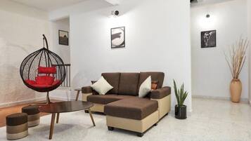A modern living room with a sectional sofa, a hanging chair, a small table, and a potted plant.