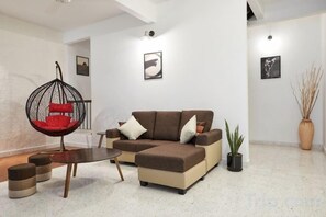 A modern living room with a sectional sofa, a hanging chair, a small table, and a potted plant. - IpohGarden Homestay, 4-12pax 10mins to attraction (Ipoh)