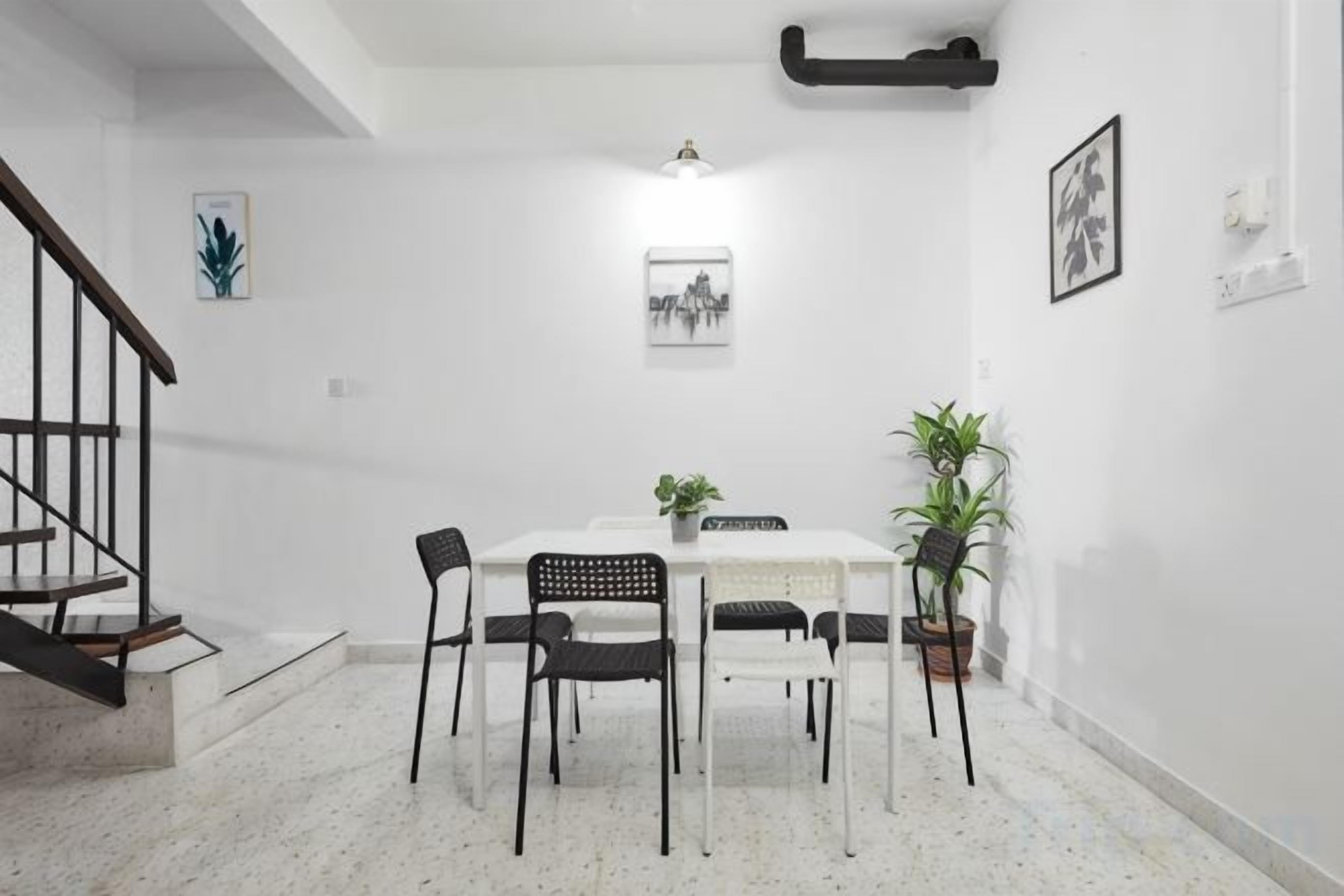 A dining area with a white table and chairs, a staircase, and a potted plant.