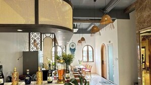 Zona de bar con mostrador que exhibe diversas botellas, una planta grande y lámparas de ratán colgantes.
