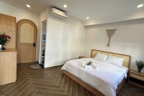 A hotel room with a bed, a wooden desk, an air conditioning unit, and a door leading to a balcony. - VENUS HOTEL PHU QUOC (Phu Quoc Island)