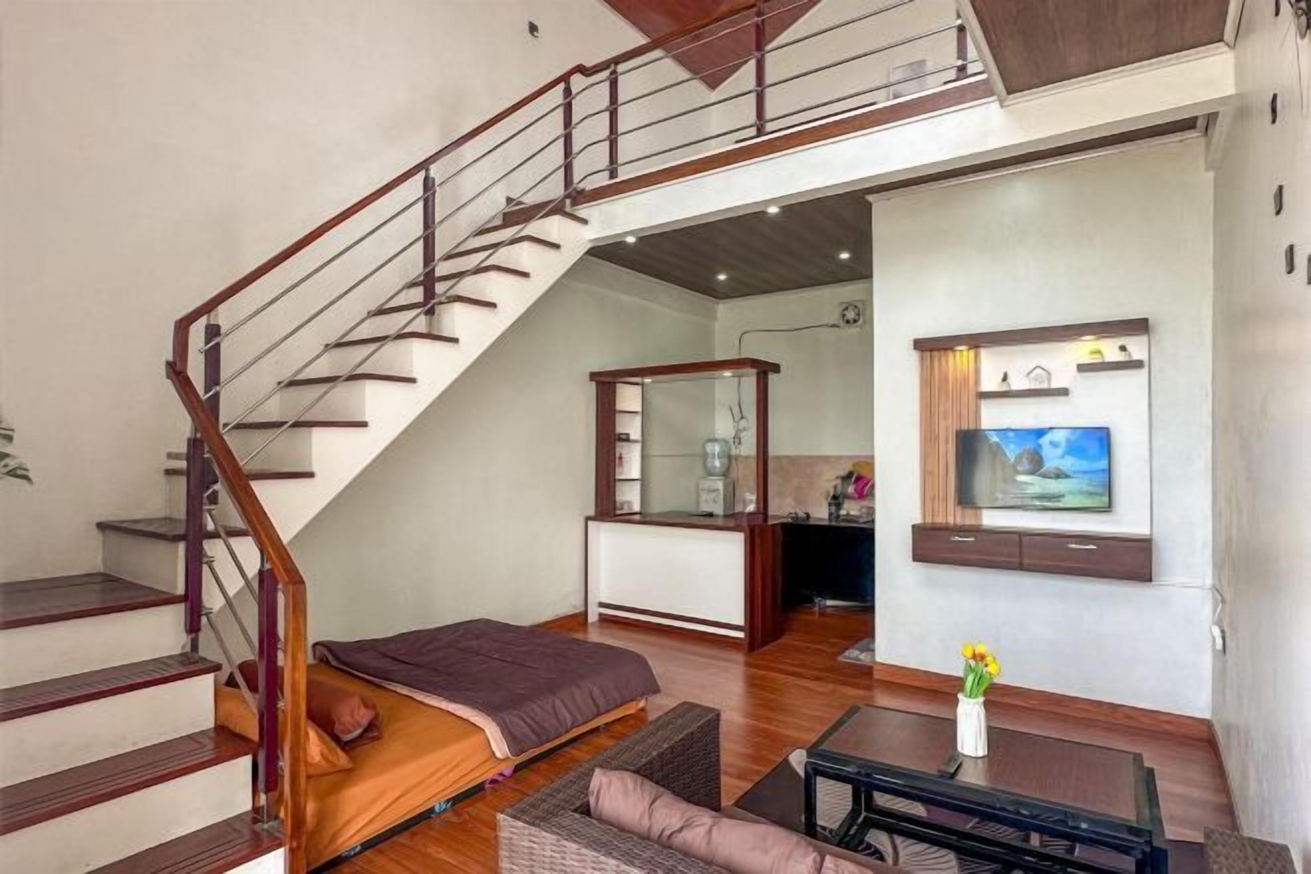 A living room with a sofa, a coffee table, a TV mounted on the wall, and a staircase leading to an upper level.