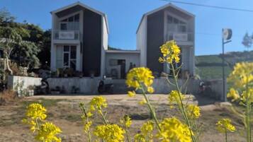 A two-story building with a balcony on the upper floor, surrounded by yellow flowers.