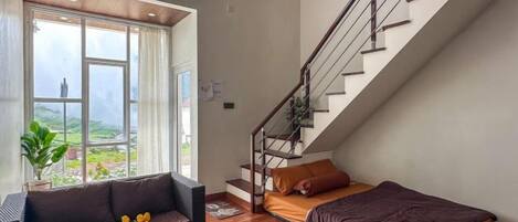 Un interior moderno con una escalera, un sofá, una cama y vistas a zonas verdes.