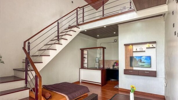 A spacious living area with a staircase, a bed, a TV mounted on the wall, and a small kitchen area. - Skypiea dieng (Batur)