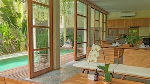 A spacious room with large sliding glass doors, wooden furniture, and a view of a swimming pool. - 2 Bedroom Villa Avyathi (Bali)