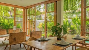 A wooden dining table with chairs, large windows, and potted plants. - 2 Bedroom Villa Avyathi (Bali)