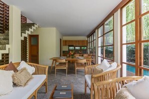 Une pièce comprenant une table à manger, des chaises, un canapé et une grande fenêtre donnant sur un paysage verdoyant.