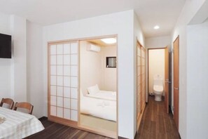 A room with a sliding shoji screen door leading to a bed, a small table with chairs, and a toilet in the adjacent room. - Sumiyoshinoyado (Osaka)