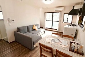 A compact living space with a sofa, dining table, chairs, a kitchenette, and a large window.