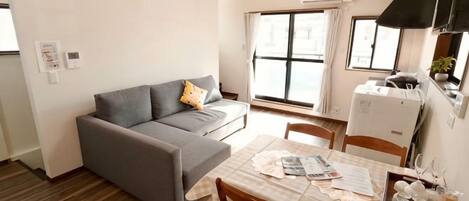A compact living space with a sofa, dining table, chairs, and a kitchenette.