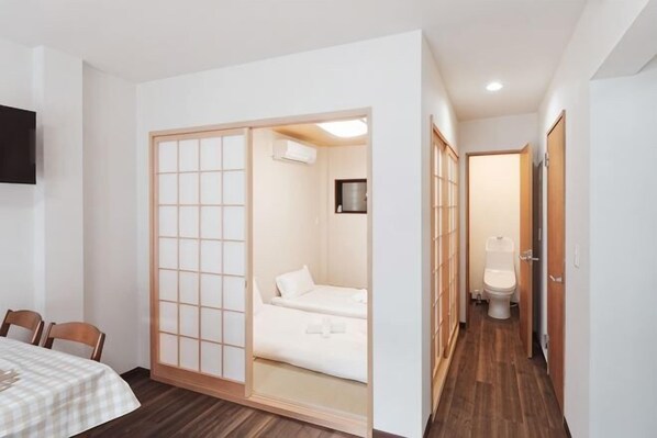 A room with a sliding shoji screen, a bed, a toilet, and a TV mounted on the wall.