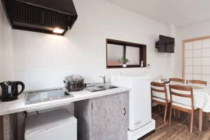 Een functionele keuken met een spoelbak, fornuis en koelkast, een eettafel met stoelen, en een aan de muur bevestigde televisie.