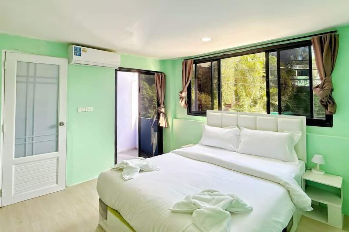 A bedroom with a bed, a bedside table, a window with curtains, and an air conditioning unit.