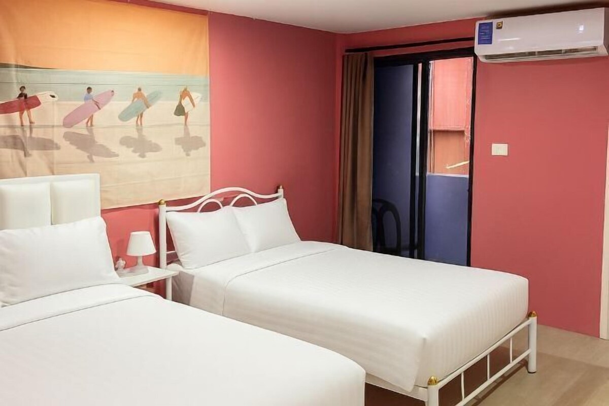 A hotel room with two beds, a wall-mounted air conditioner, and a view of a beach scene.