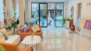 A modern hotel lobby with a sofa, chairs, a small table, and easels with paintings. - Chen inn Boutique House Patong (Phuket)