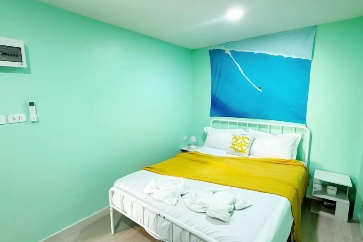 Una habitación con una cama, una mesita de noche, un aire acondicionado instalado en la pared y un cuadro de un cielo azul.