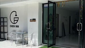 A modern hotel entrance with a glass door, a sign reading "CHEN INN," and a small outdoor seating area with chairs and a table. - Chen inn Boutique House Patong (Phuket)