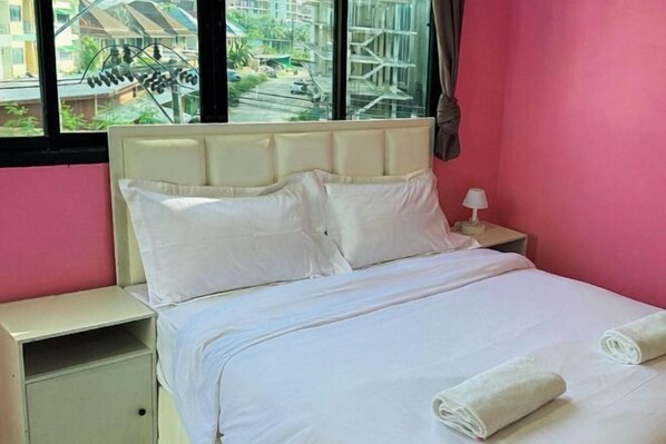 Habitación de hotel con cama, mesita de noche, lámpara y ventana que ofrece vistas a edificios y zonas verdes.