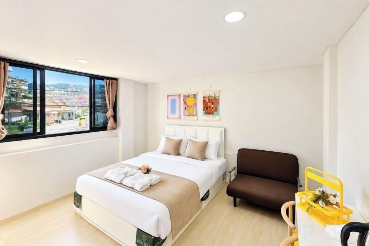 Une chambre d’hôtel avec un lit, un canapé, une fenêtre donnant sur la ville et une petite table sur laquelle se trouve un plateau jaune.
