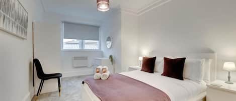 A bedroom with a bed, bedside table, chair, and a window.