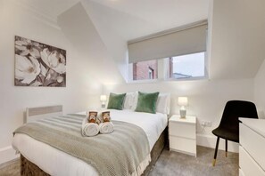A bedroom with a bed, bedside tables, a chair, a window, and a painting on the wall. - Hudson's Haven Apartment- By Week2Week (Newcastle)