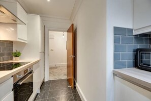 A compact kitchen with a microwave, oven, and a small countertop with a plant. - Hudson's Haven Apartment- By Week2Week (Newcastle)