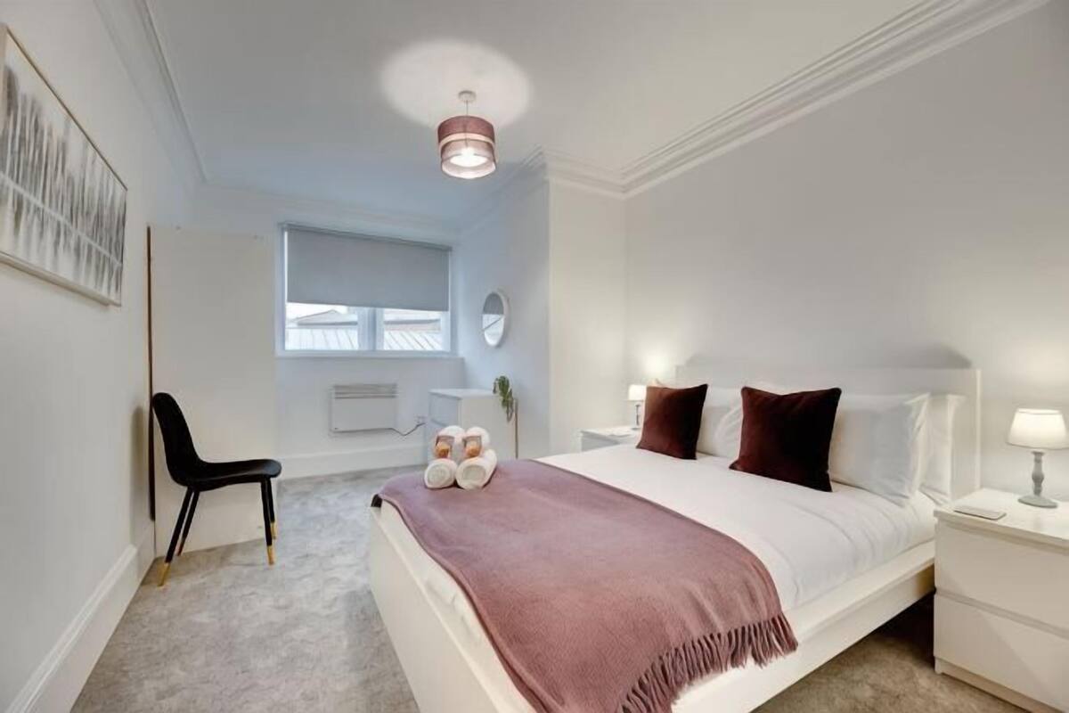 A bedroom with a bed, bedside table, chair, and a window.