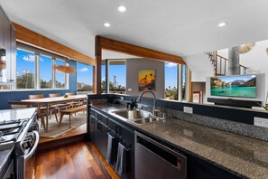 Cocina moderna con encimera de granito, pileta de acero inoxidable y comedor con sillas y mesa de madera.