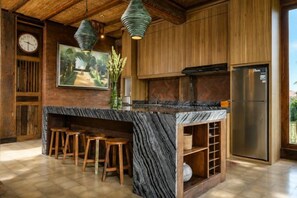 A kitchen with a marble island, wooden stools, a clock, and a refrigerator. - The Joglo at Umah Sunset (Bali)