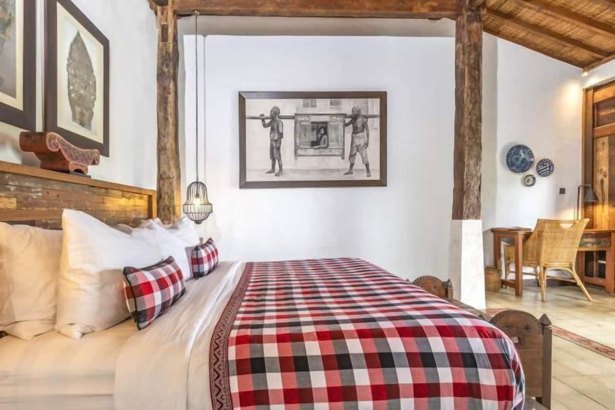 A bedroom with a bed, pillows, a checkered blanket, a framed picture, and a wooden chair.